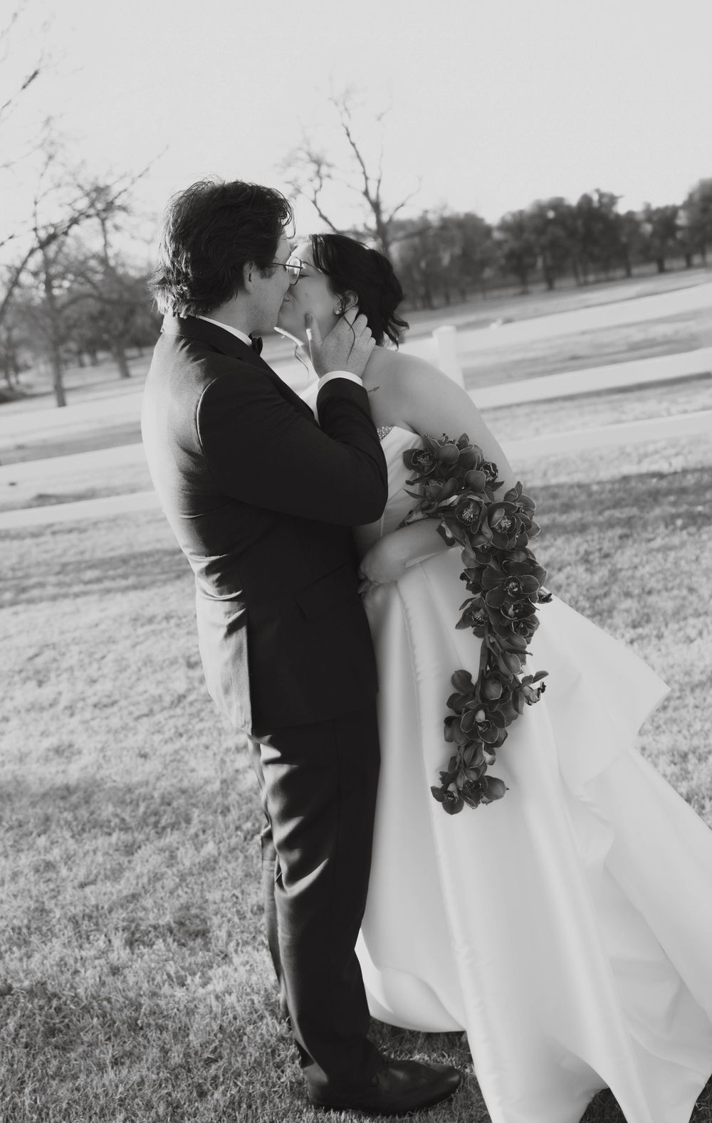 Black and white photo of bride and groom sharing a passionate kiss outdoors on their wedding day.