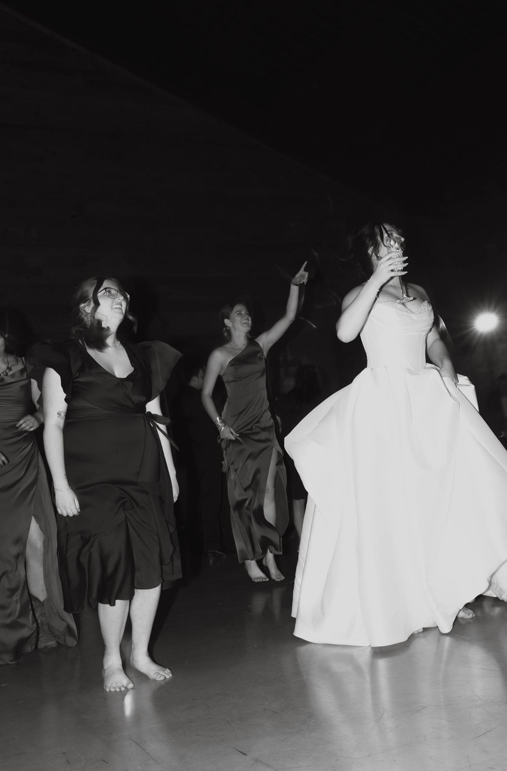 Black and white photo of bride and bridesmaids dancing barefoot at wedding reception.