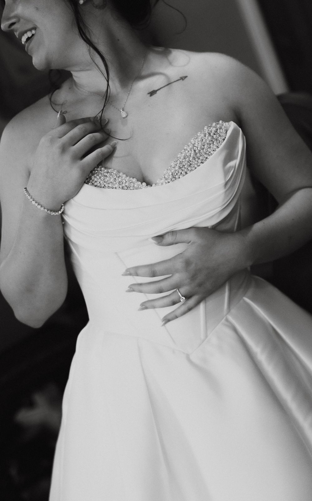 Black and white close-up of a smiling bride in a strapless beaded wedding dress with pearl bracelet.