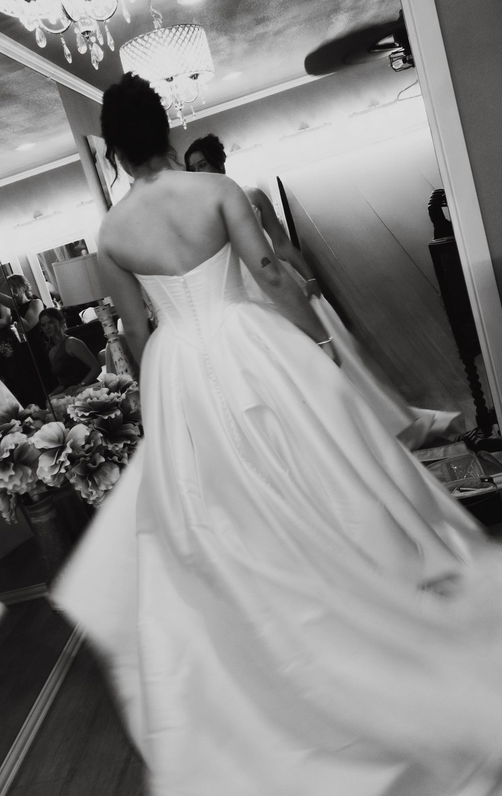 Black and white photo of a bride in a full ball gown wedding dress viewed from behind in a mirrored bridal shop.