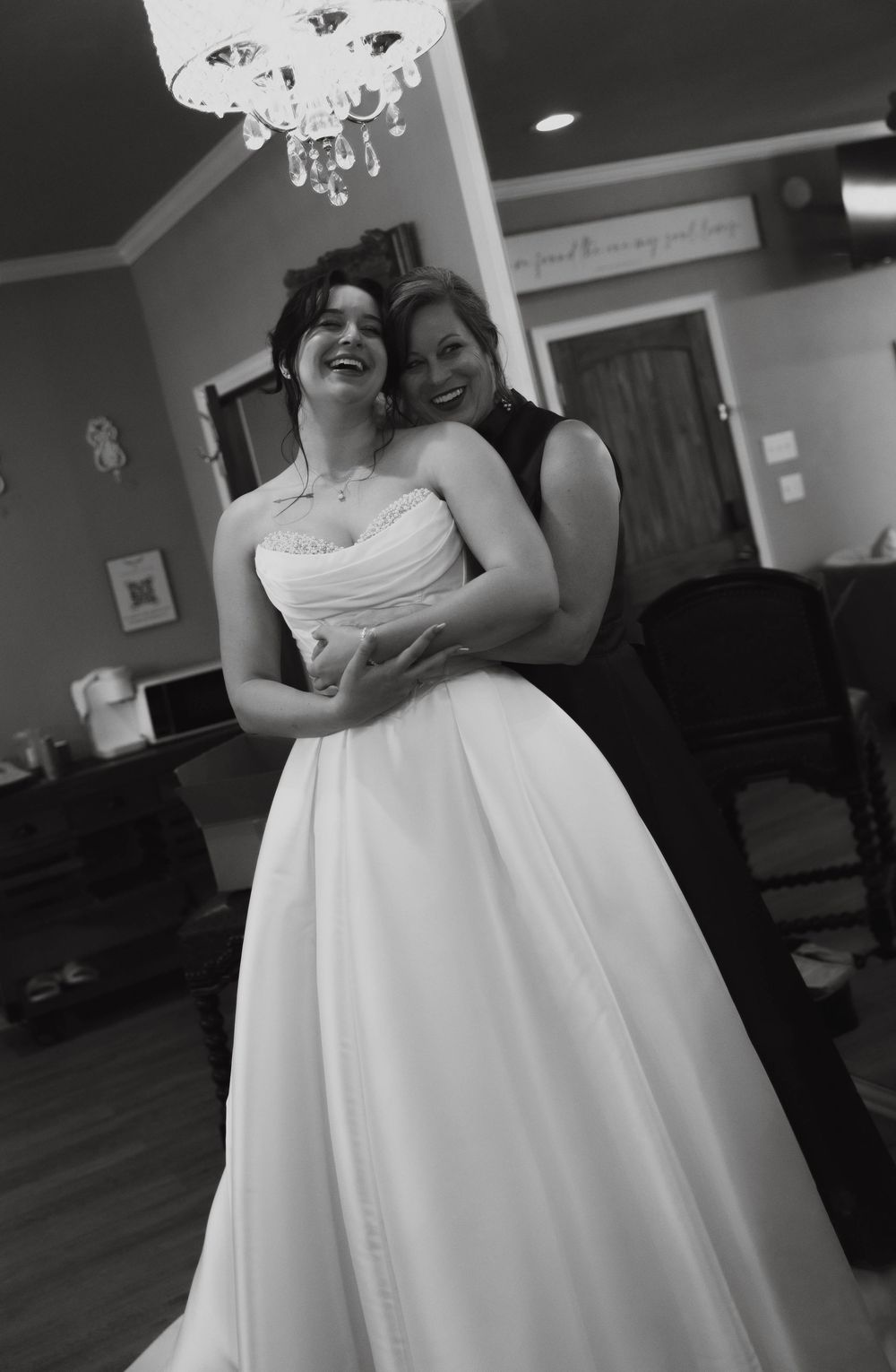 Black and white photo of a laughing bride in a strapless ball gown being embraced by a smiling woman.