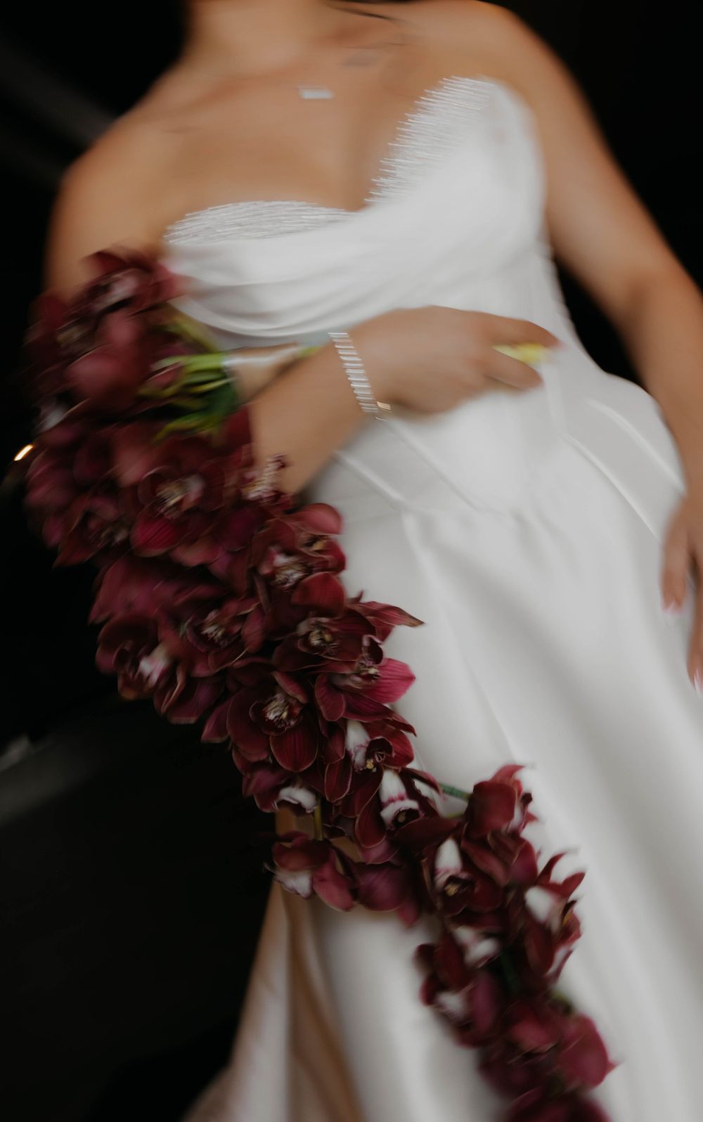 Motion-blurred close-up of bride in white strapless gown carrying cascading deep red orchid bouquet.