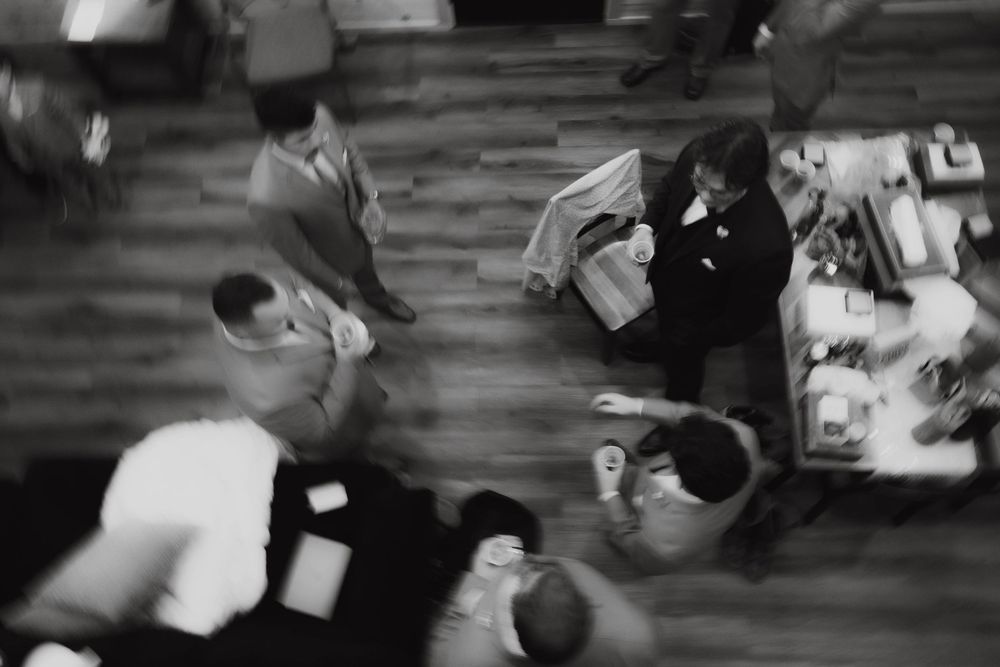 Black and white aerial view of wedding reception guests mingling on wooden dance floor.