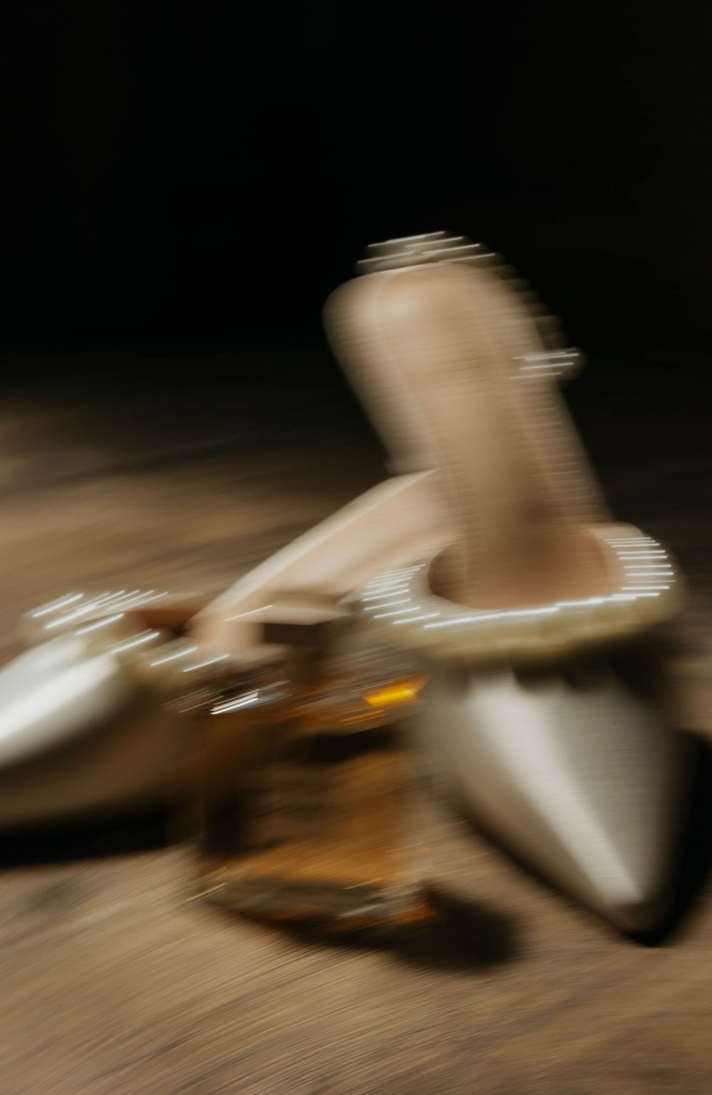 Artistic motion blur photo of pearl-trimmed bridal shoes and perfume bottle in warm tones.