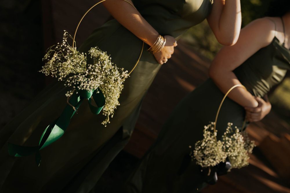Bridesmaids in sage green dresses holding delicate baby's breath hoop bouquets with green ribbons.