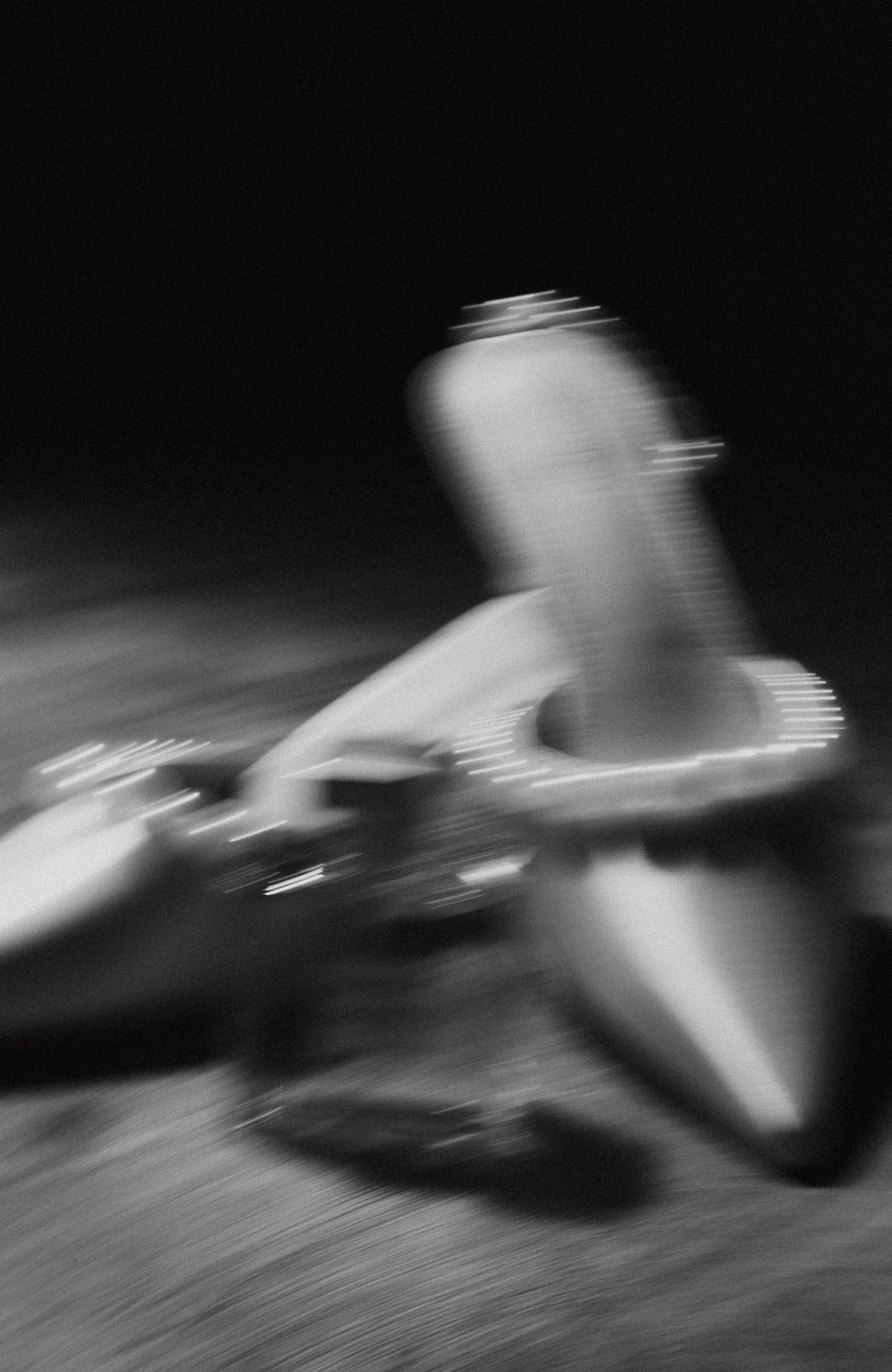 Black and white motion blur artistic shot of pearl-trimmed bridal heels and perfume bottle.