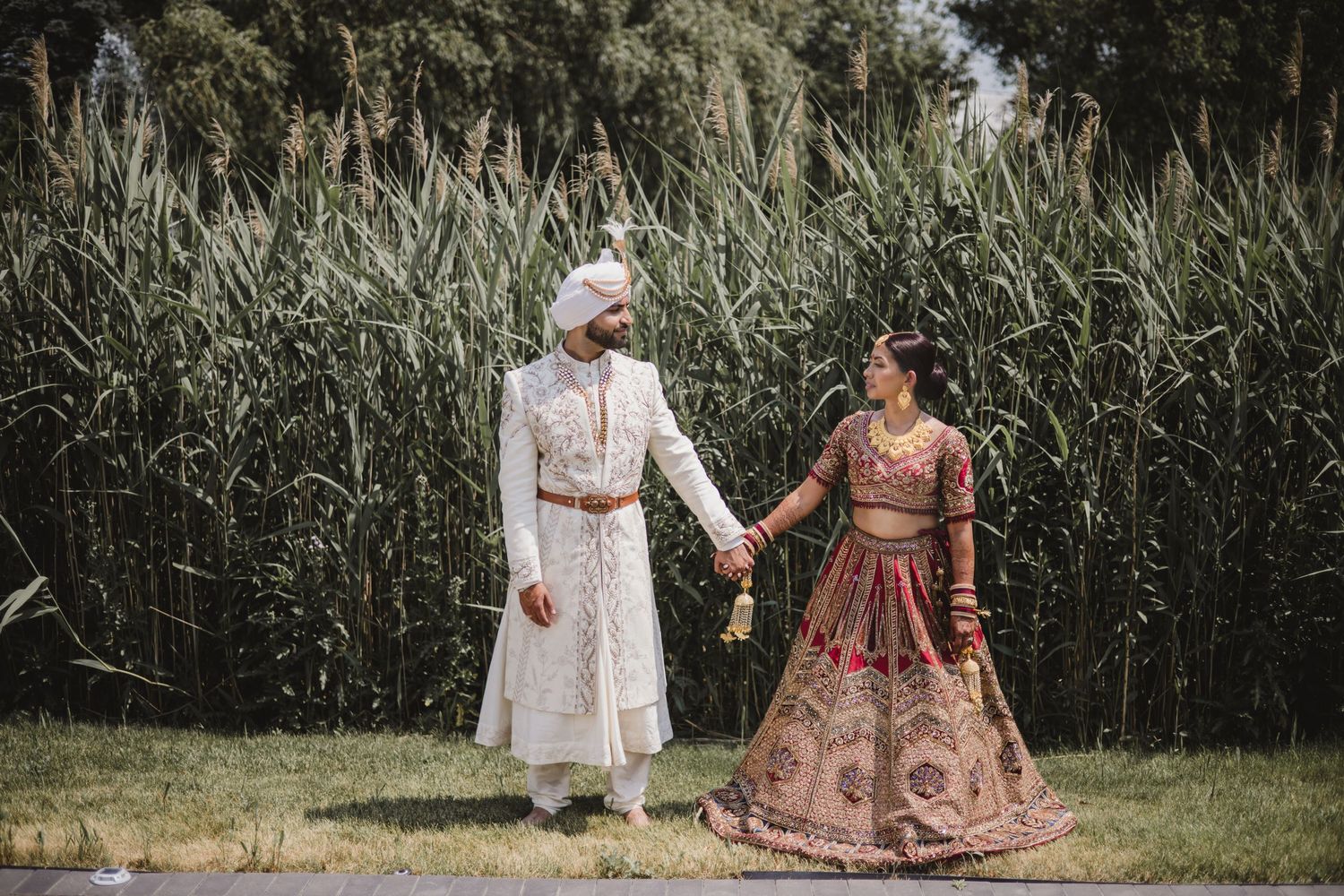 Two people walk together through a tall grass field wearing elegant vintage-style dresses in summer light.