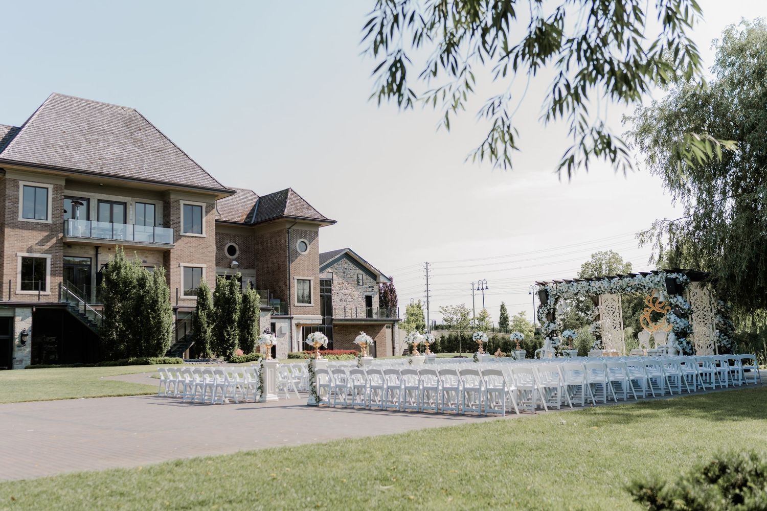White chairs arranged in rows for an outdoor wedding ceremony with luxury homes and trees in the background.