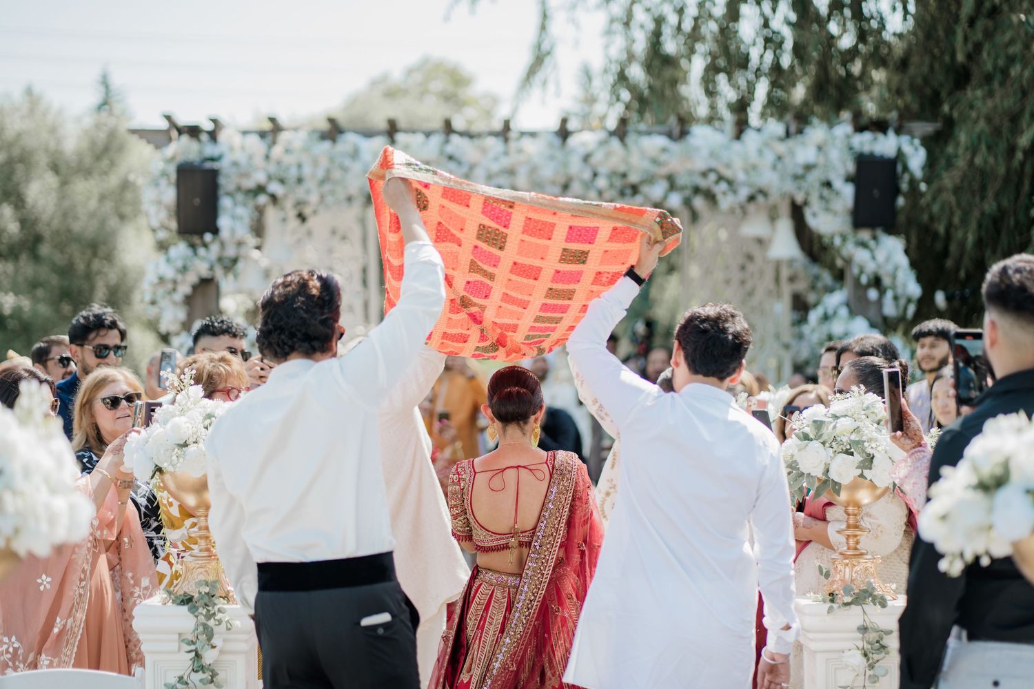 A wedding celebration with guests in traditional Indian attire gathering outdoors under natural lighting.
