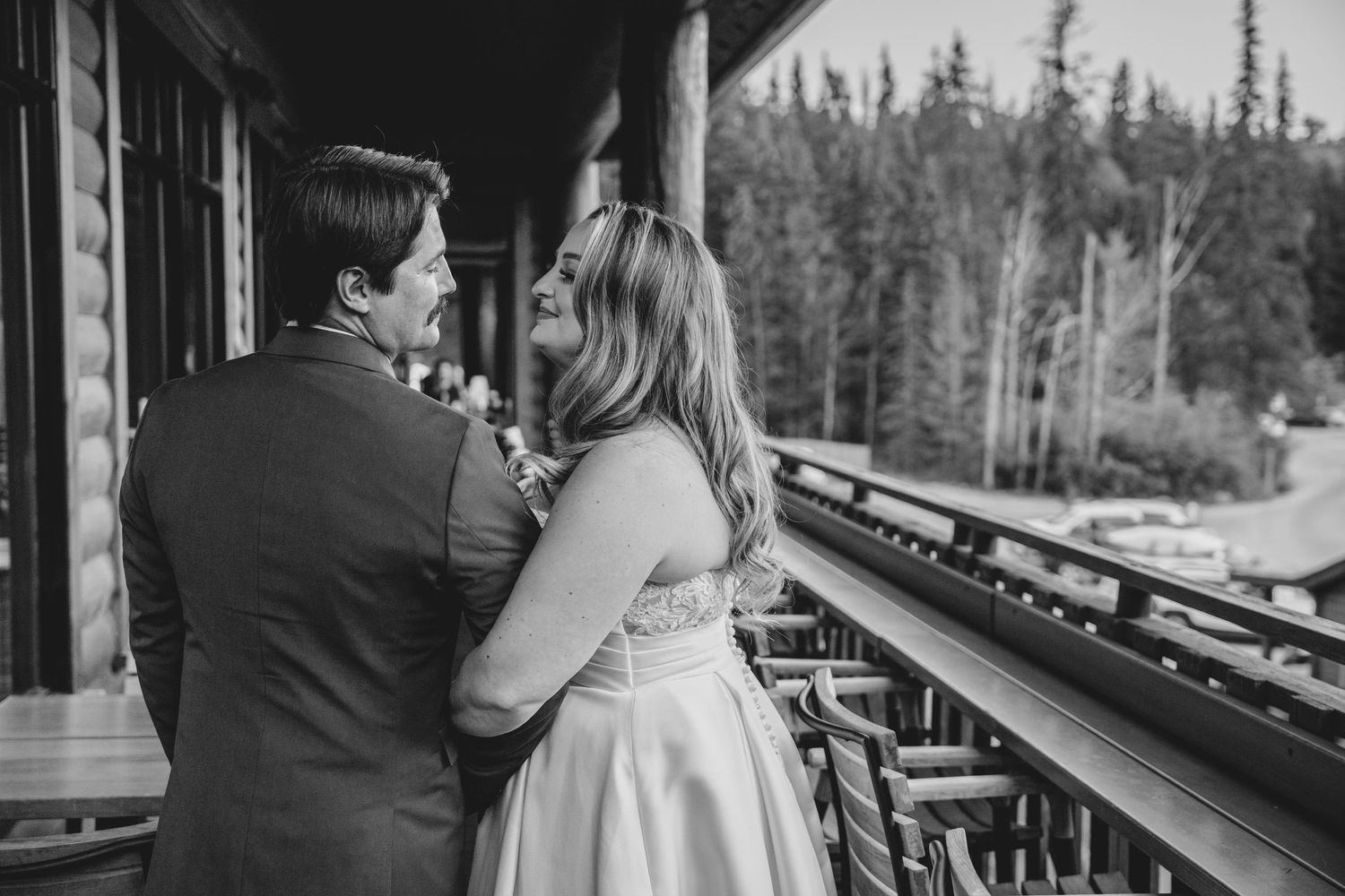 Couple sharing an intimate moment by a window in a rustic cabin with evergreen trees visible outside.