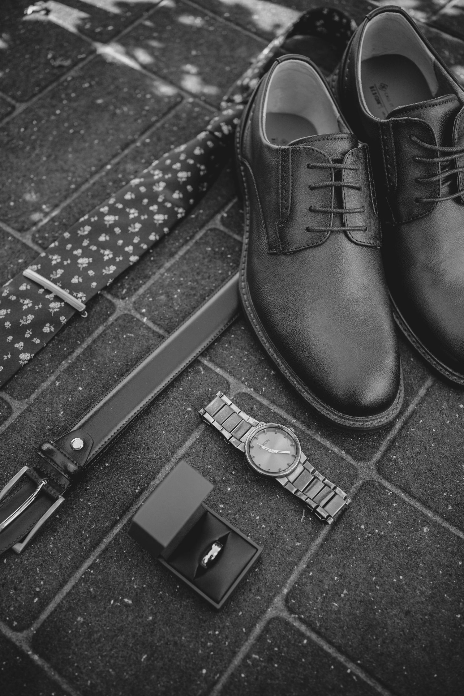 Black dress shoes and accessories including a watch and wallet arranged on a textured surface.