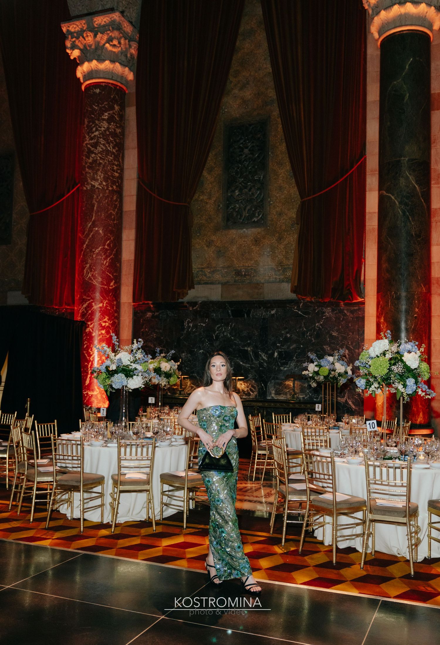 Elegant wedding reception venue with white chairs and floral centerpieces illuminated by dramatic red lighting.