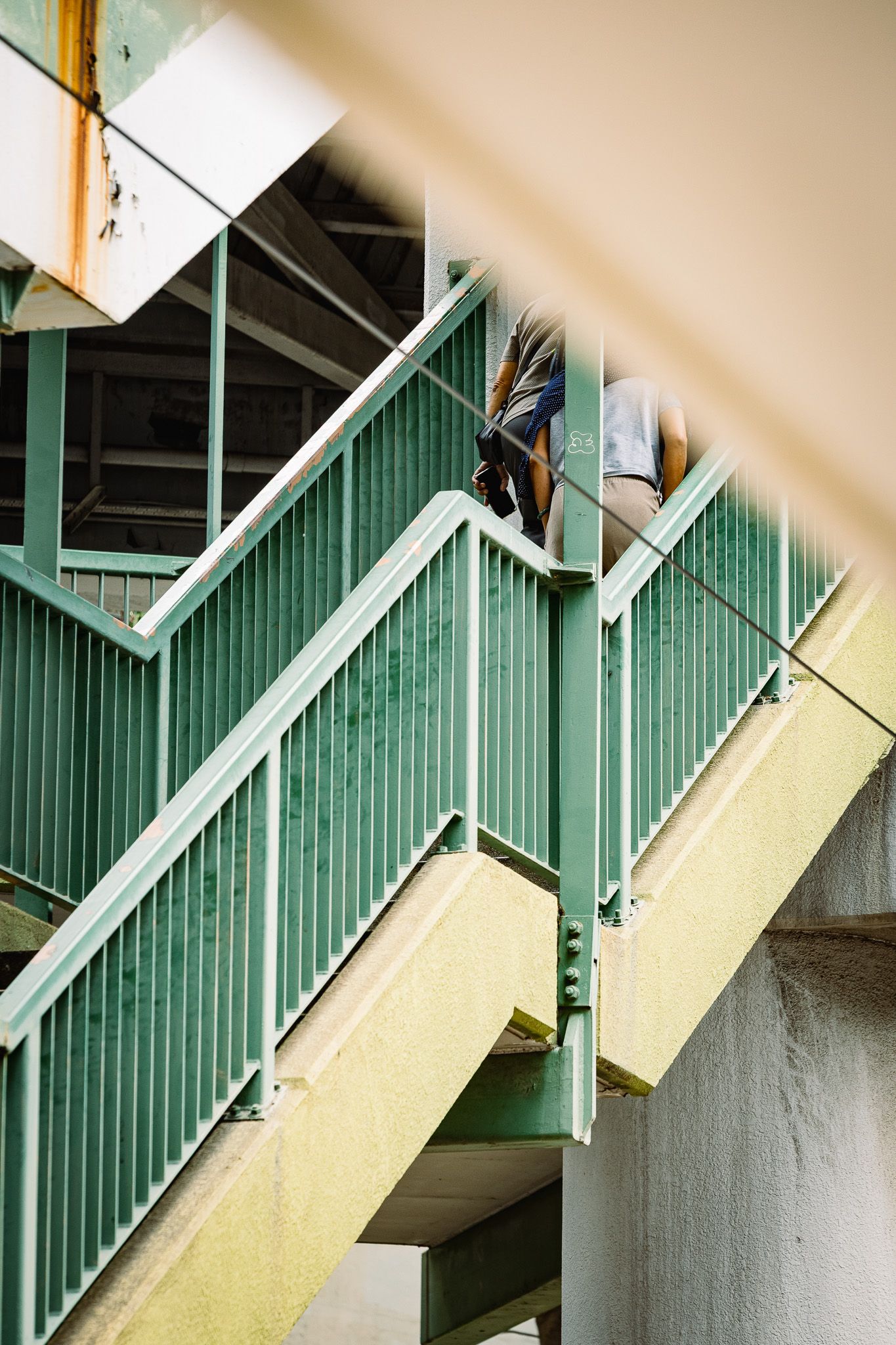 Person descending weathered green metal fire escape stairs in an urban building exterior.
