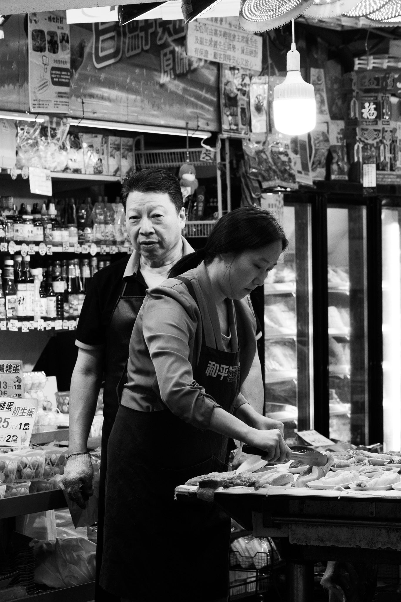 Two women working at a food stall in a Hong Kong wet market in black and white photography.