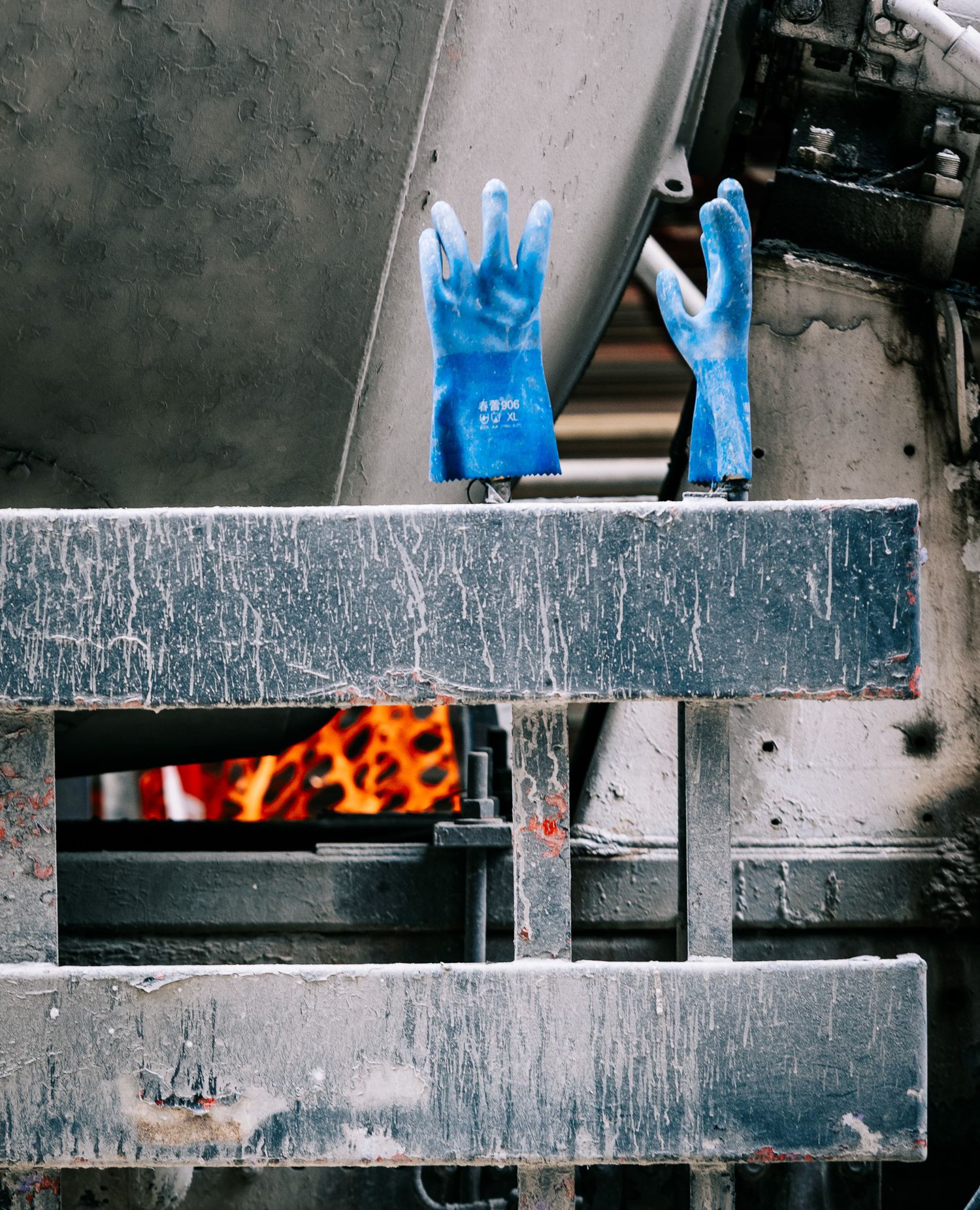 Blue rubber safety gloves resting on metal industrial equipment with glowing fire visible below.