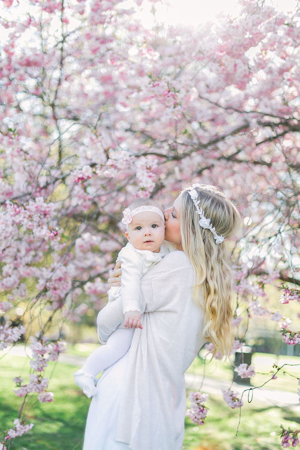 Barn- och familjefotografering i Stadsträdgården, Karlstad. Angelina håller i bebis-Melissa med glosor runt dem. Pussar henne på kinden.