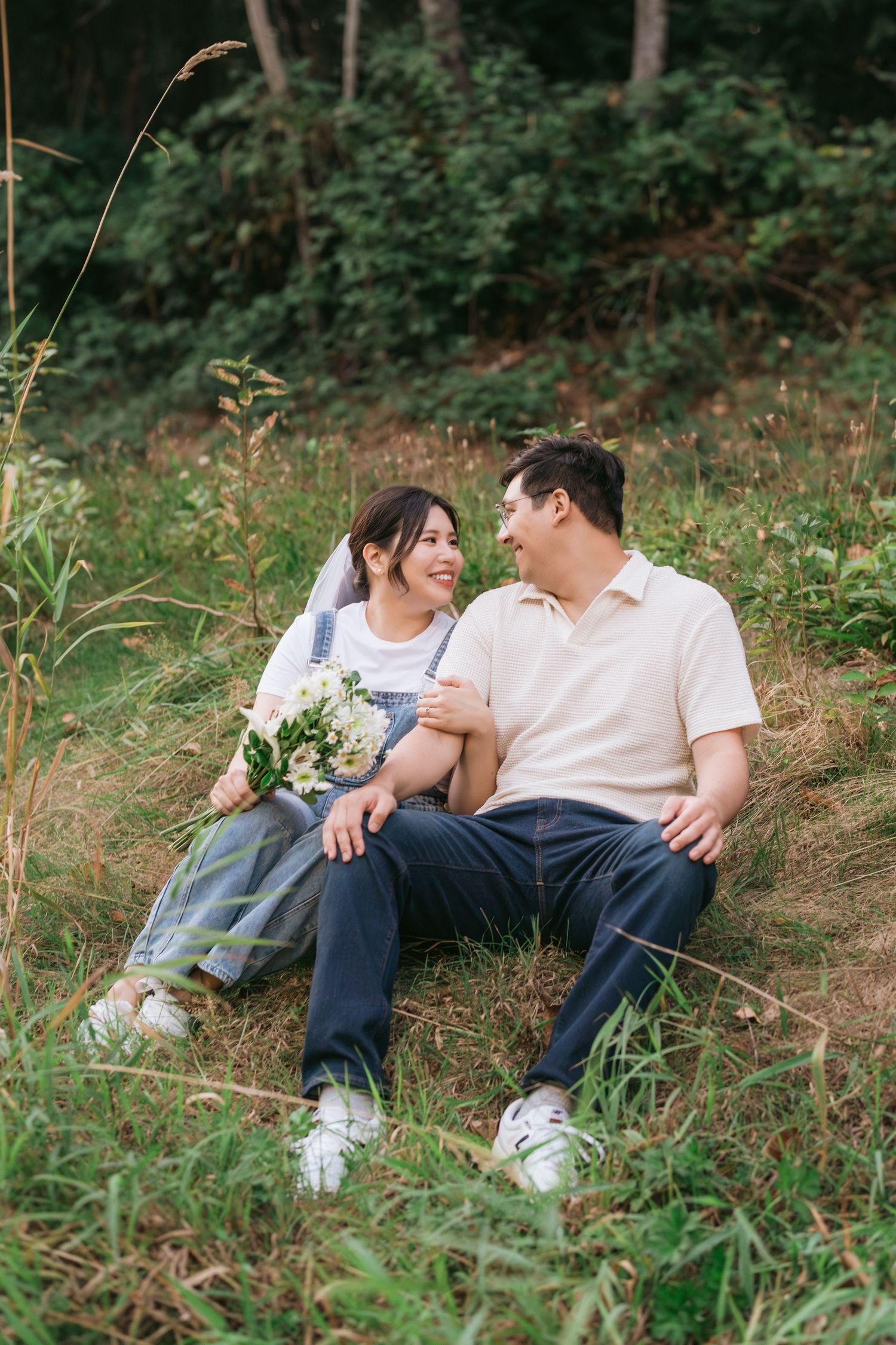 A couple relaxes together on grassy hillside during casual outdoor photo session.