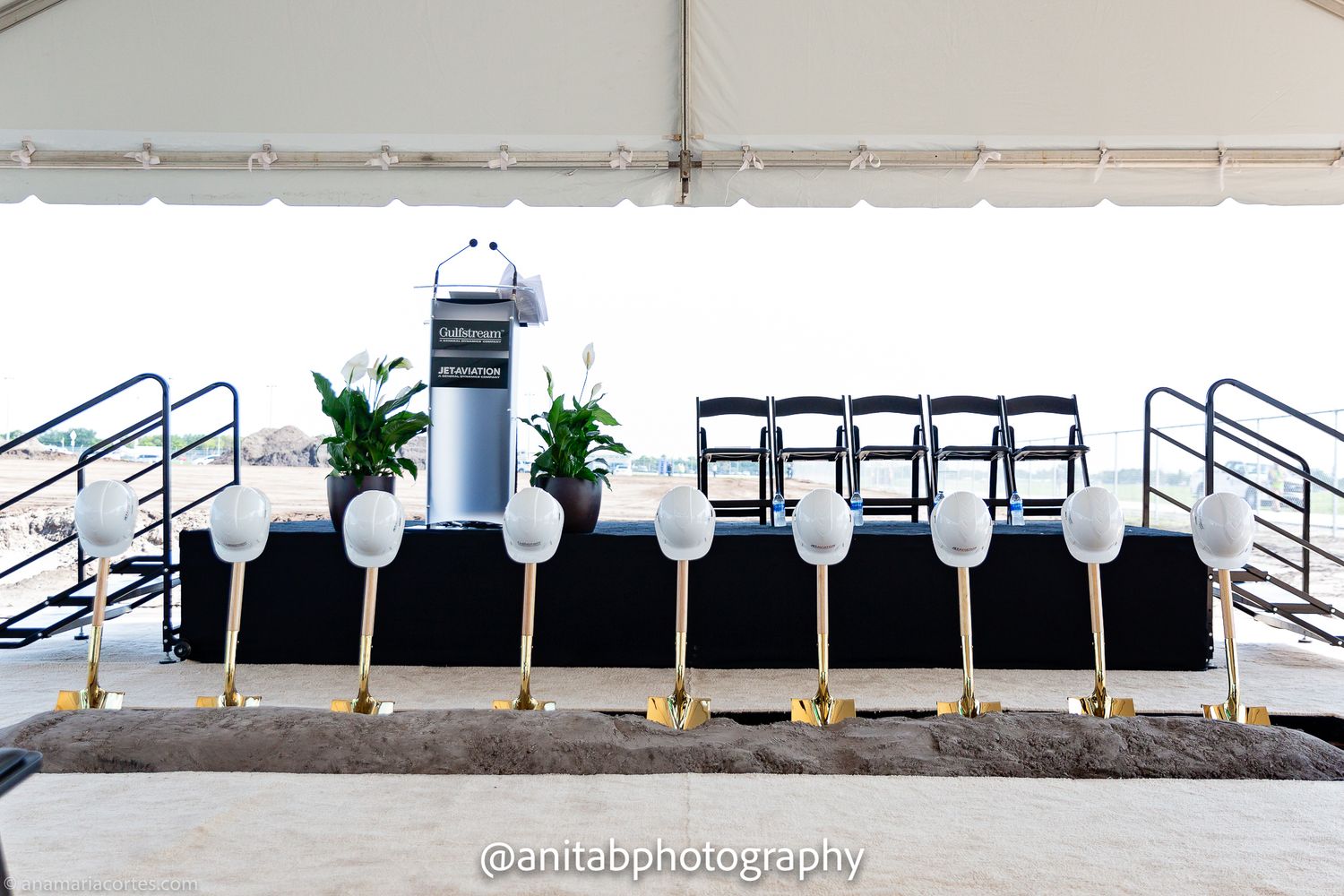 Row of empty white chairs arranged under an outdoor tent.
Braking ground event.