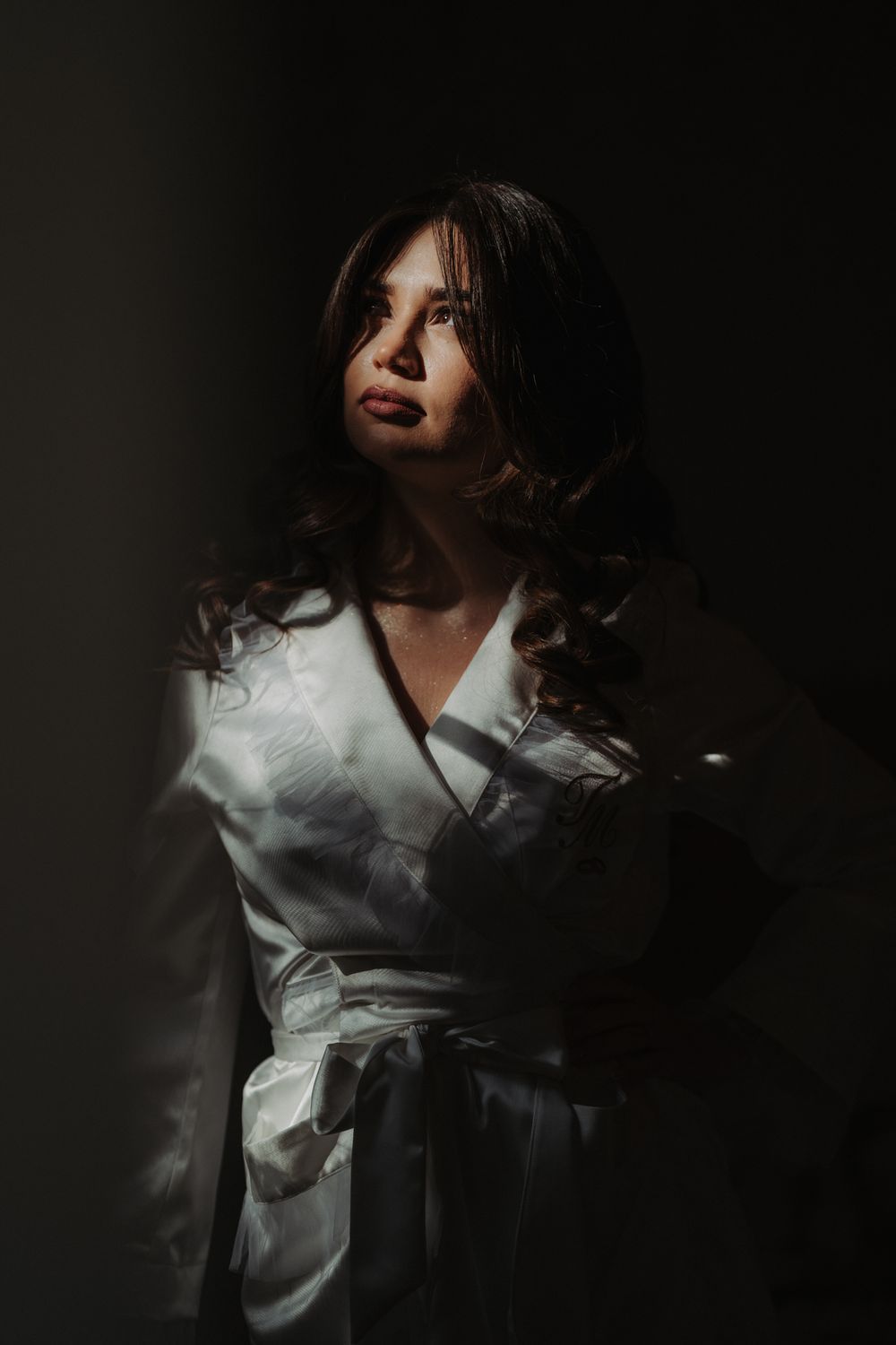 Dramatic low-key portrait of figure in white robe against dark background with moody lighting and shadows.