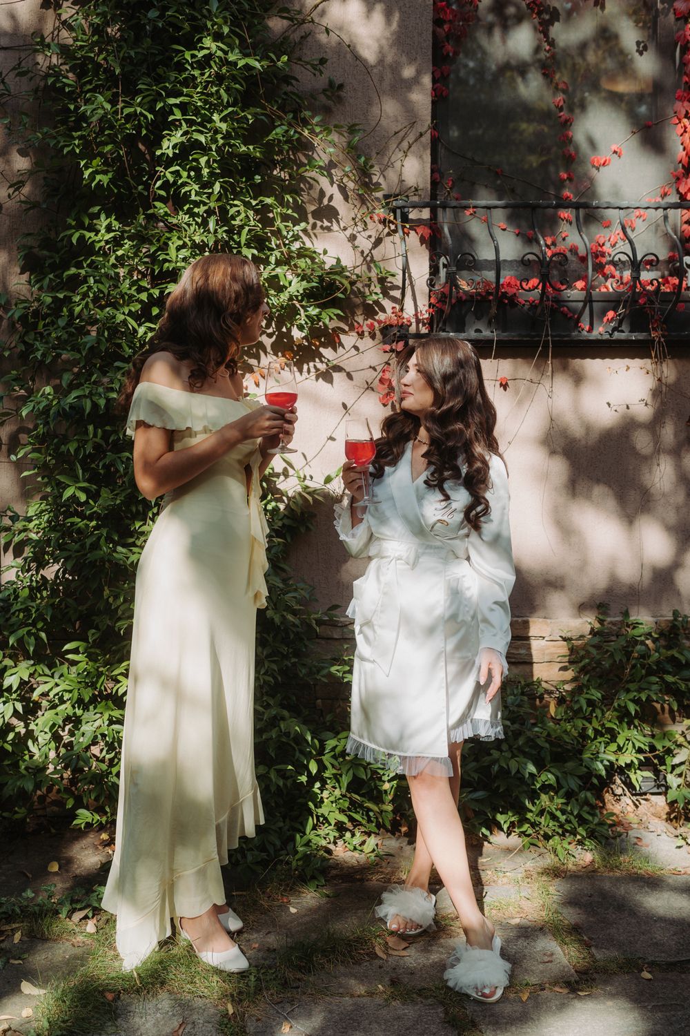 Two figures in light colored dresses dance together in a sunlit garden with dappled shadows and green foliage.