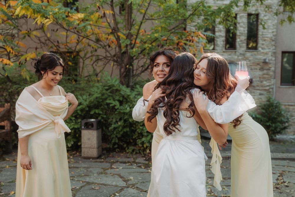 A joyful group in white dresses laughs and embraces during an outdoor autumn photoshoot.