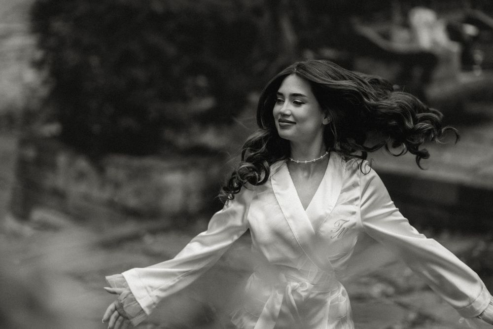 A woman in a white robe spins joyfully with flowing dark hair in a black and white photograph.