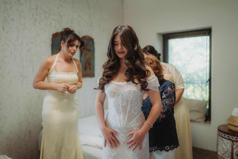 A group helps a bride get ready in a sunlit room during wedding preparations.