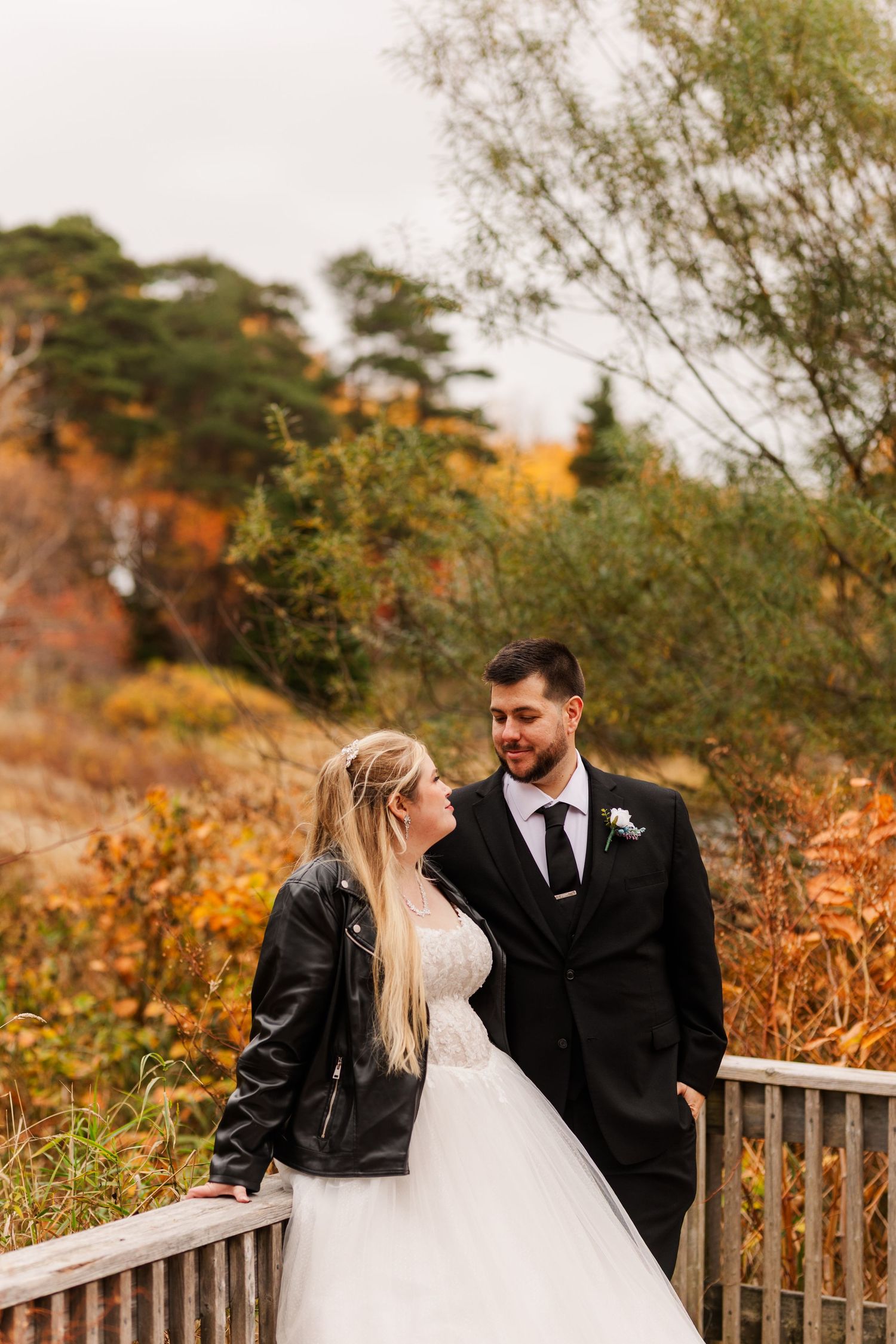 A bride and groom share intimate moments against a backdrop of golden autumn foliage and rustic fencing.