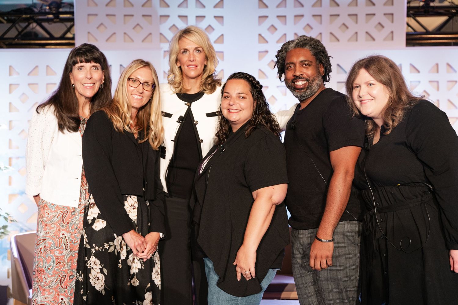 A group of people wearing black outfits pose together at a formal event against a patterned backdrop.