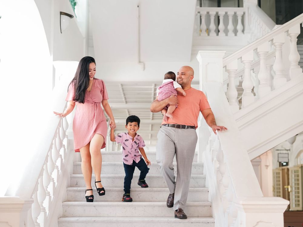 A family in coordinating pink and coral outfits poses on an elegant white marble staircase for photos.
