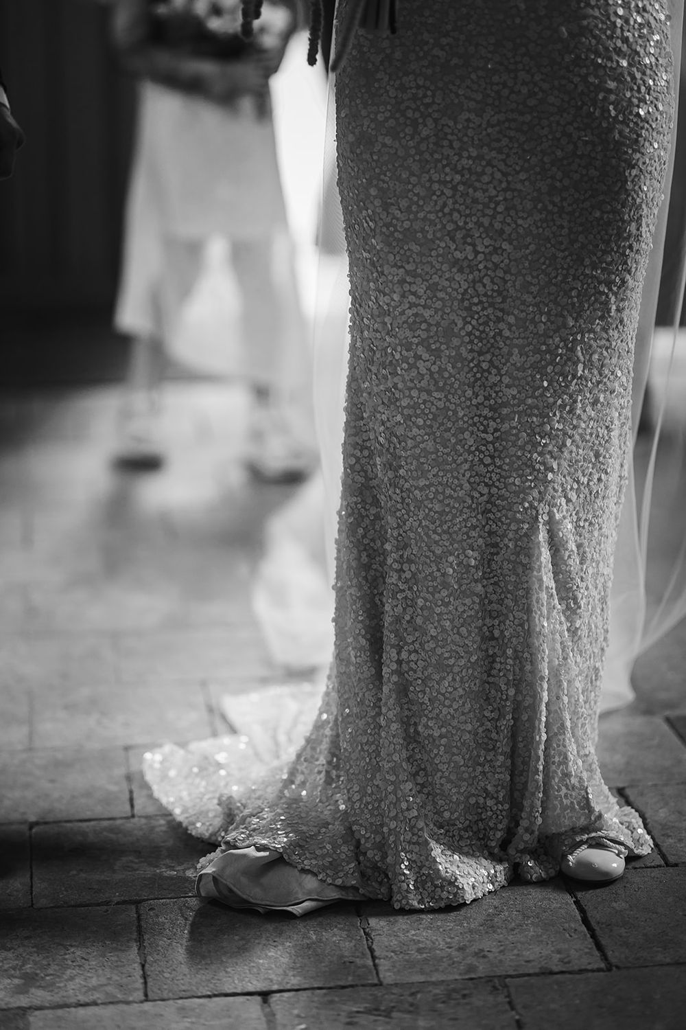 Black and white detail shots of a bride's wedding dress hem and shoes on a stone floor.