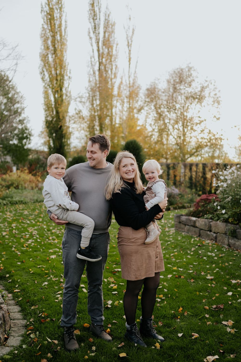 Eine Familie genießt gemeinsam einen Herbsttag auf ihrem Rasen, mit hohen Pappeln und abgefallenen Blättern im Hintergrund.