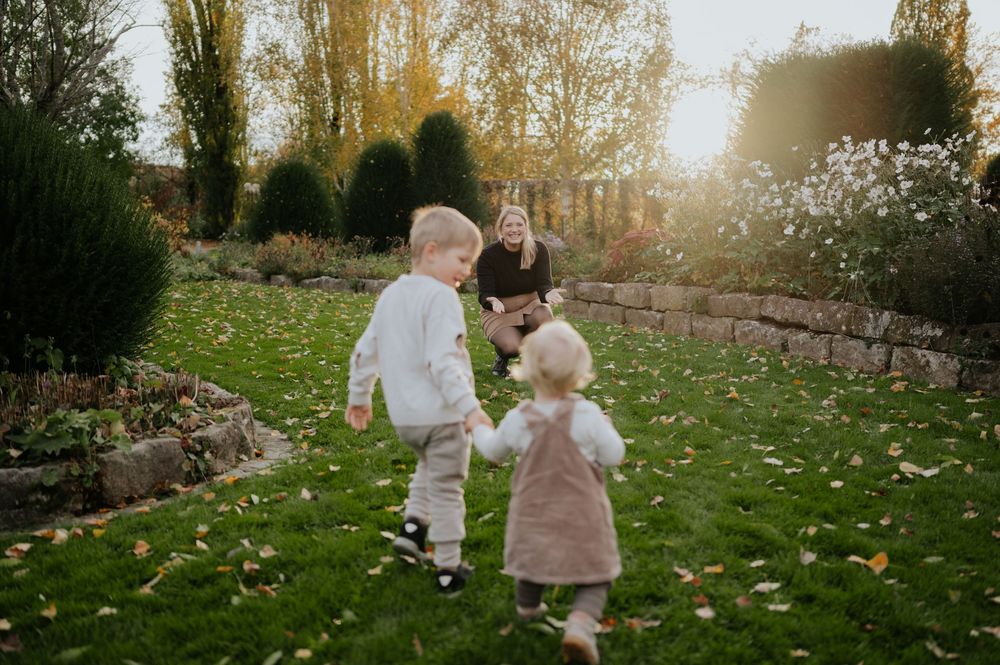 Zwei kleine Kinder in heller Kleidung spielen zusammen auf einer mit Herbstblättern übersäten Wiese.