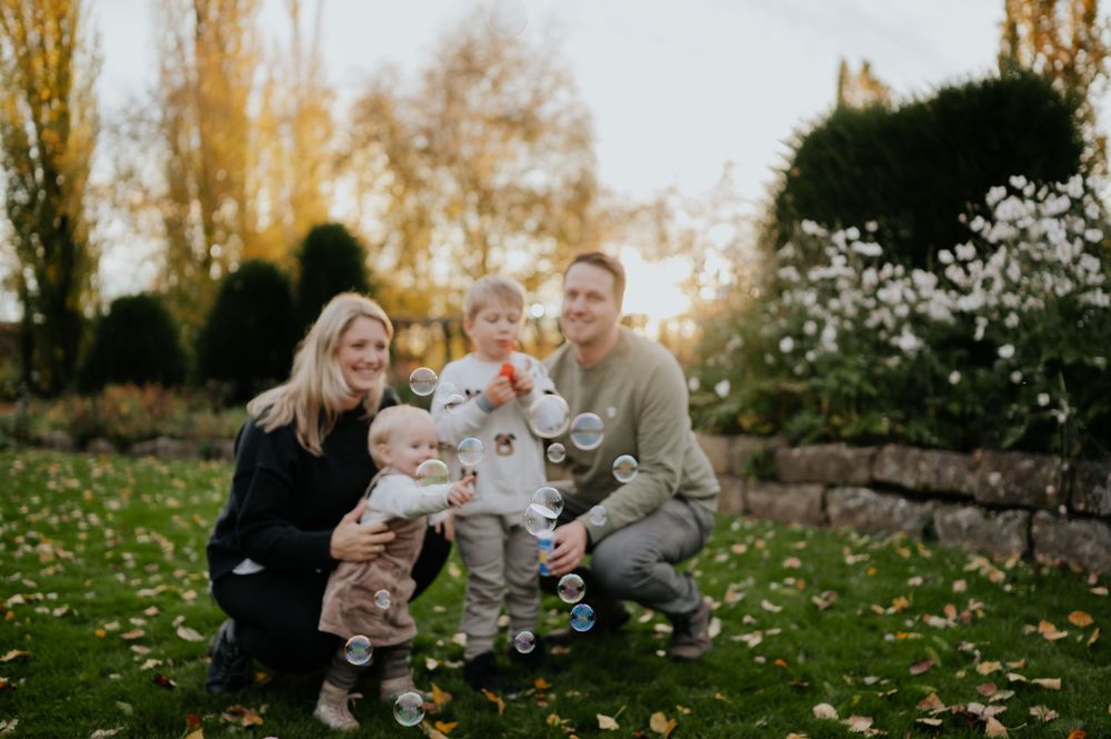 Eine Familie sitzt während eines Fotoshootings im Herbst während der goldenen Stunde gemeinsam auf dem Rasen im Park.