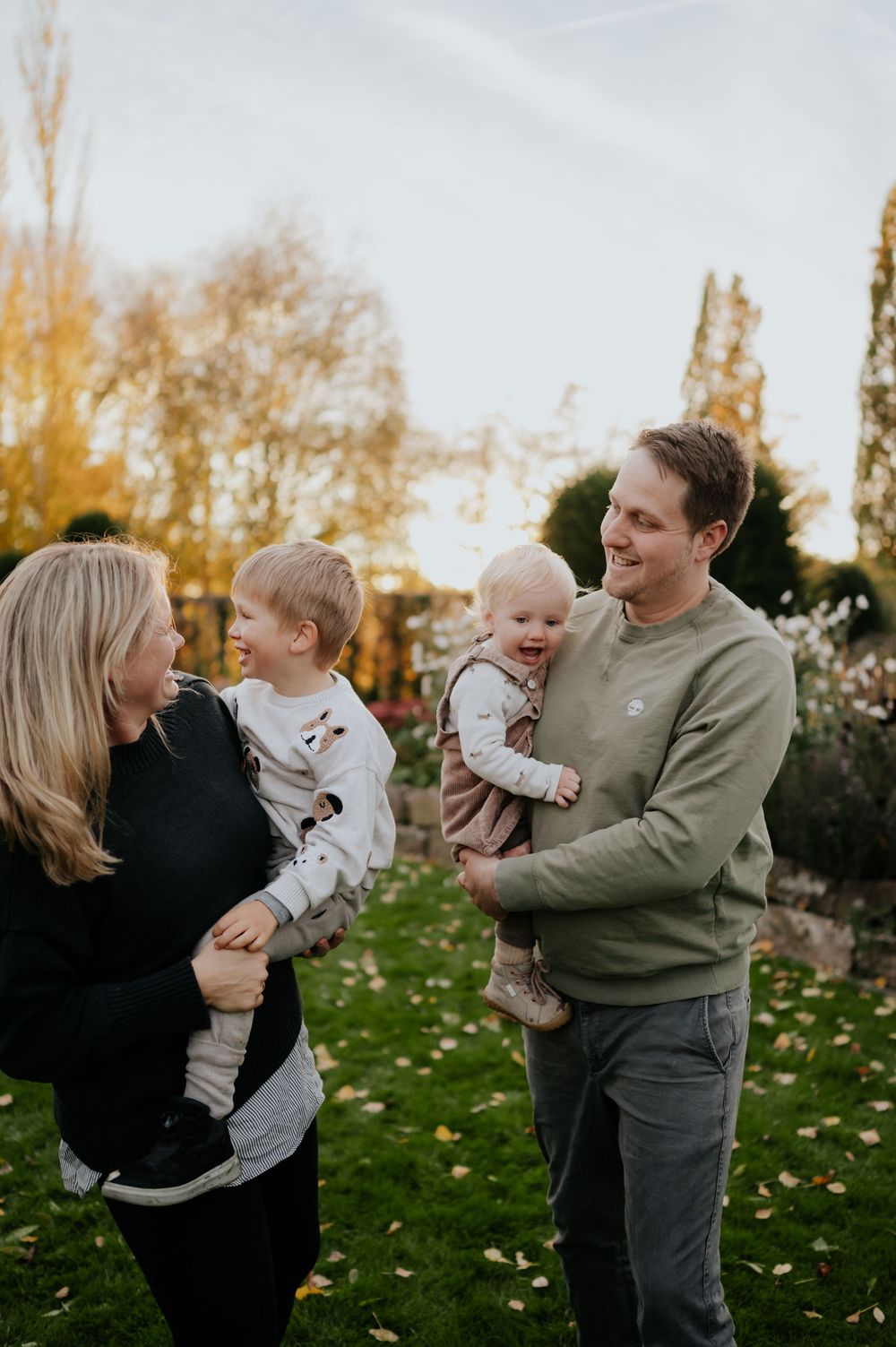 Eine Familie genießt spielerische Momente zusammen in einem Herbstgarten mit Laub und goldenem Licht.