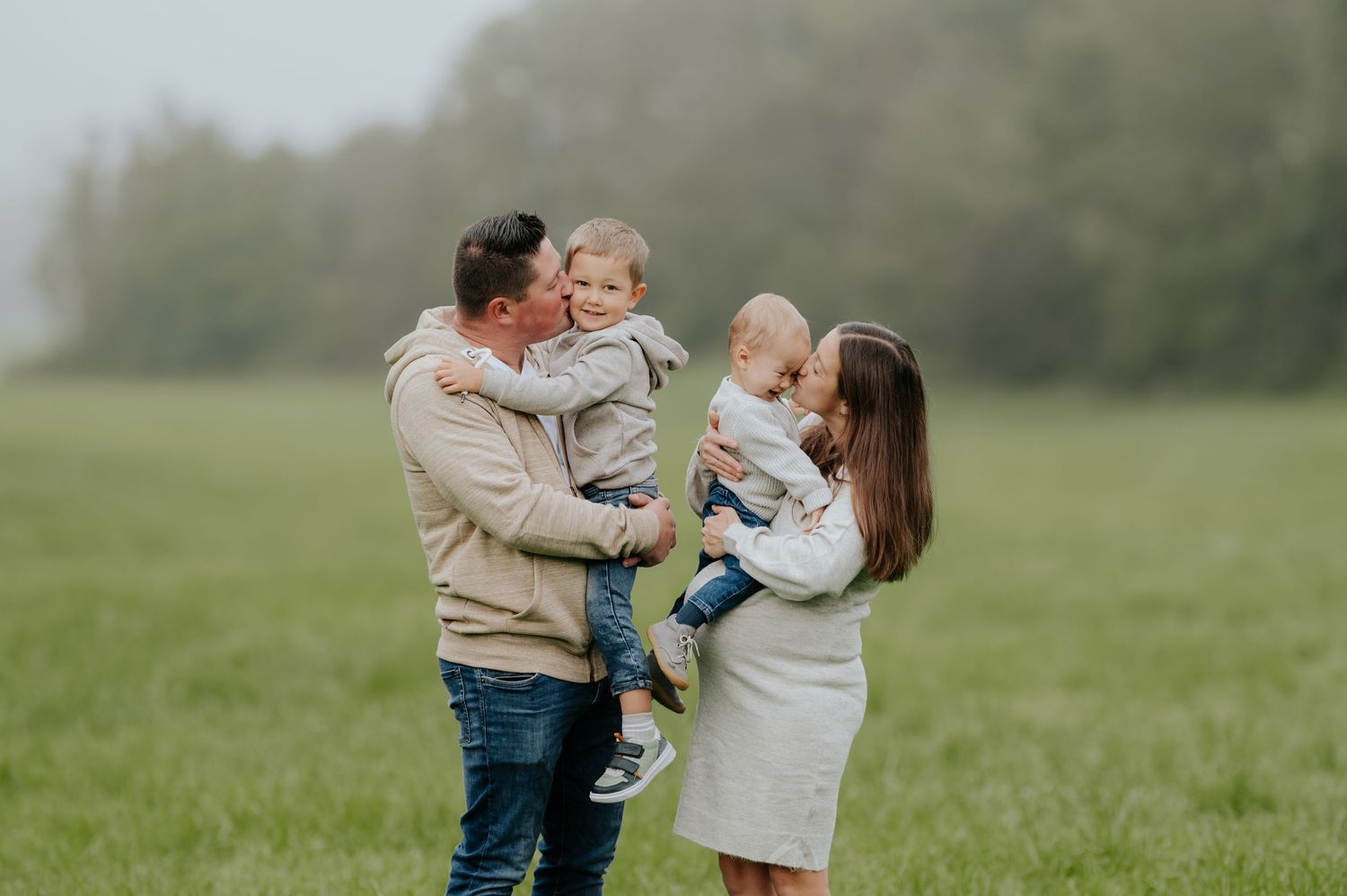 Eine Familie teilt freudige Momente auf einer grünen Wiese während einer ungezwungenen Fotosession im Freien.