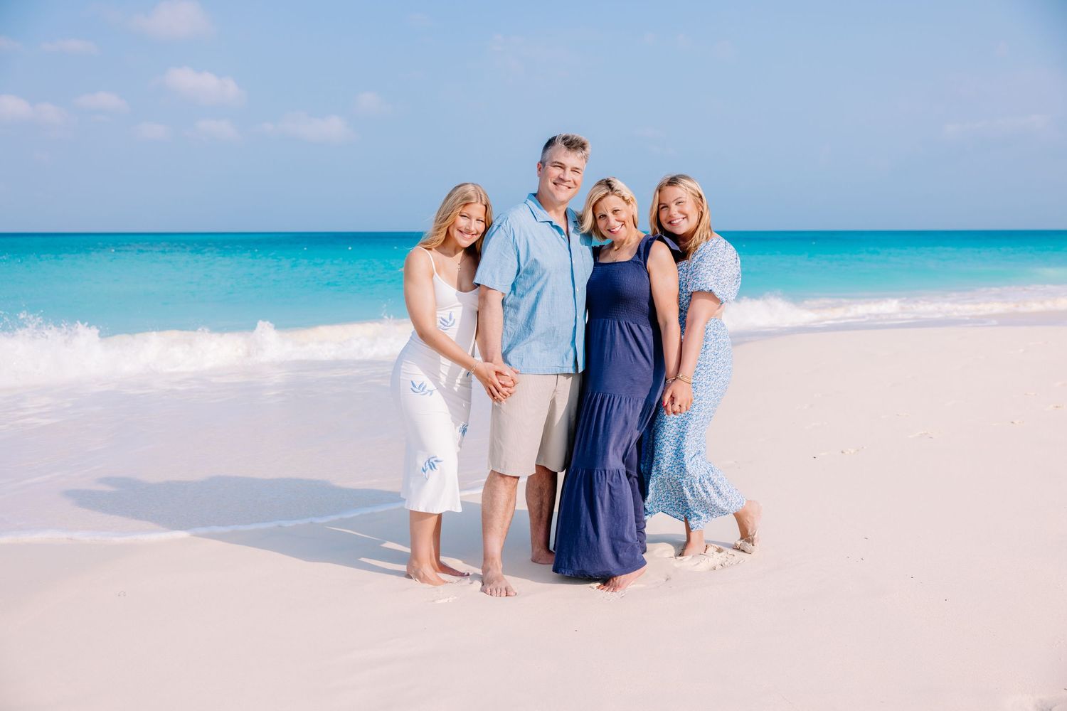 Family enjoying a beach photoshoot in coordinated blue and white outfits by the ocean.