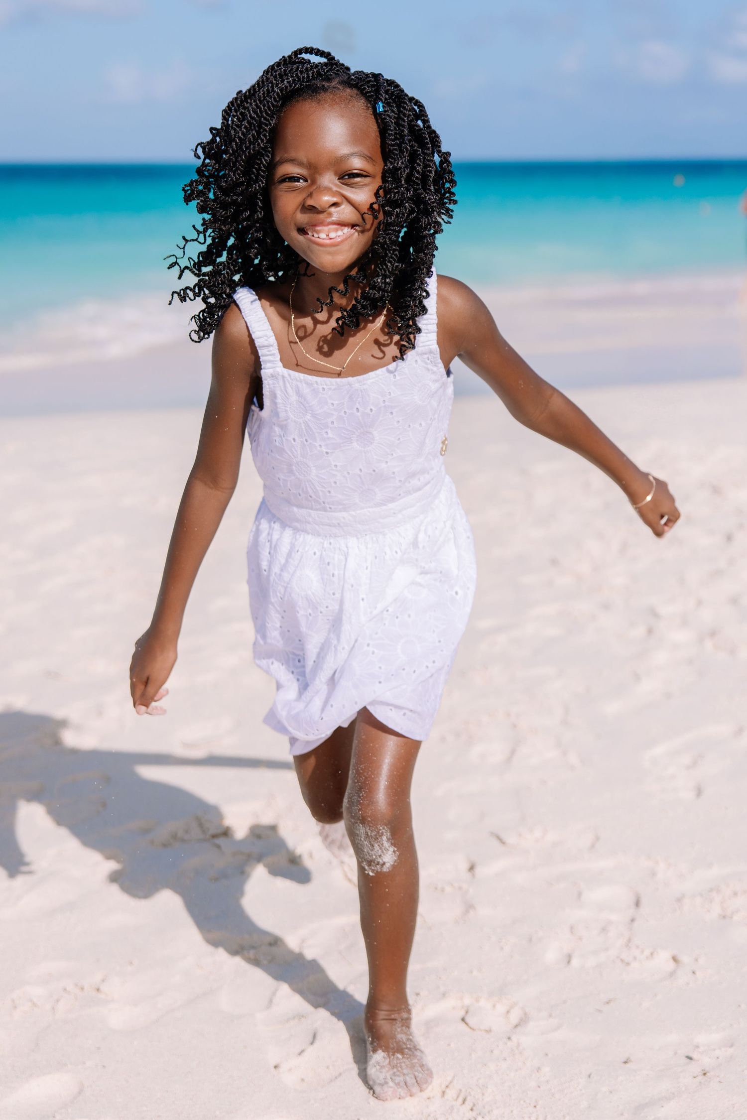 Child in a white dress runs and plays joyfully on a pristine white sand beach.