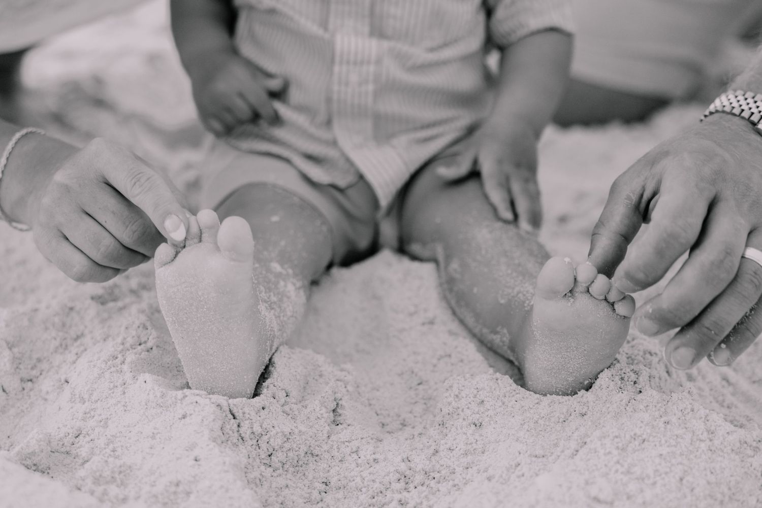 Black and white close-up of hands resting on sandy beach.