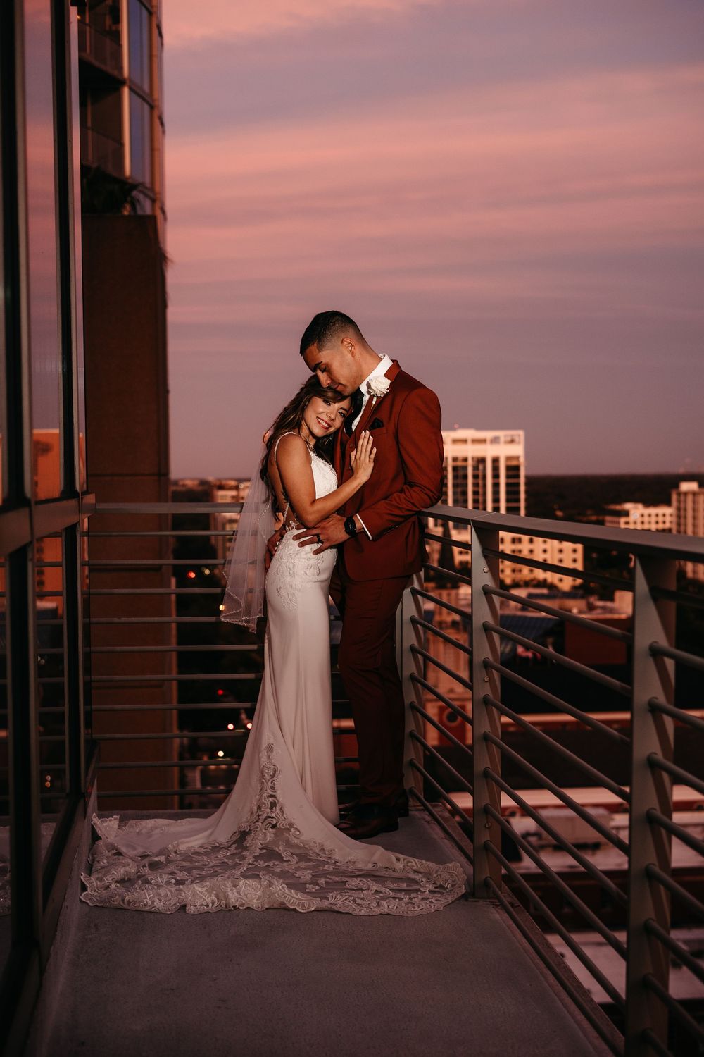 Newlyweds share intimate moments on a balcony during sunset against city skyline. Orlando downtown wedding.