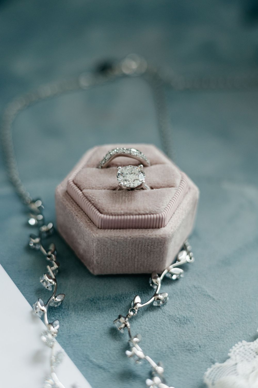 Elegant engagement ring in pink velvet ring box with delicate floral accents on teal background.