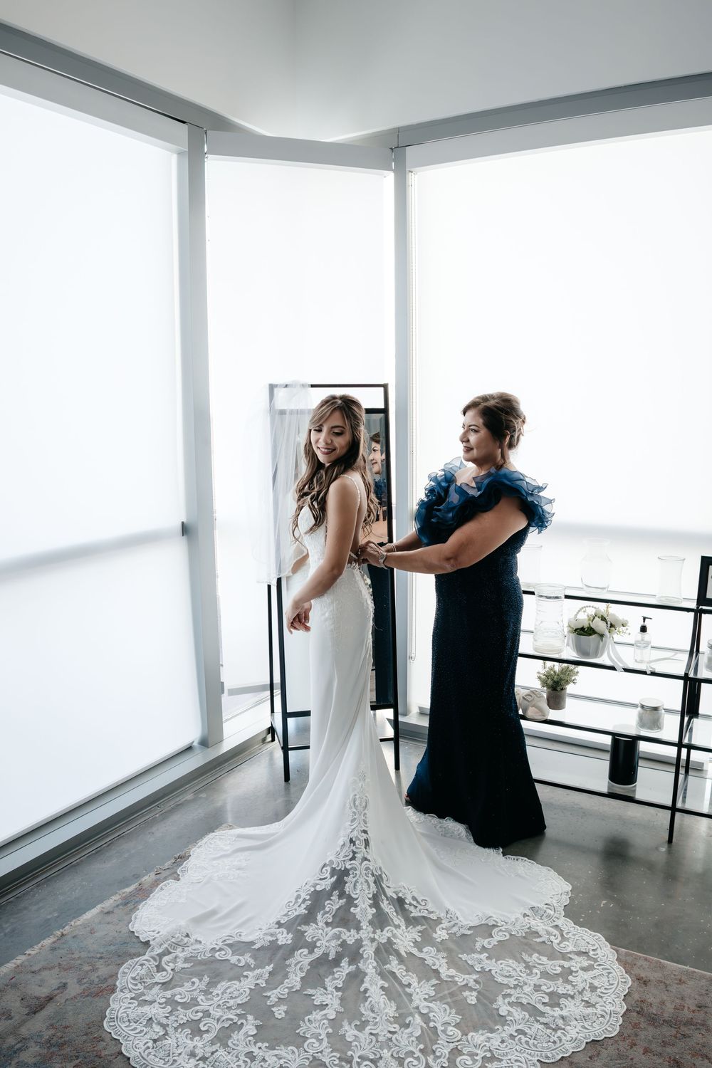 Wedding dress fitting in a modern bright room with floor-length lace train.