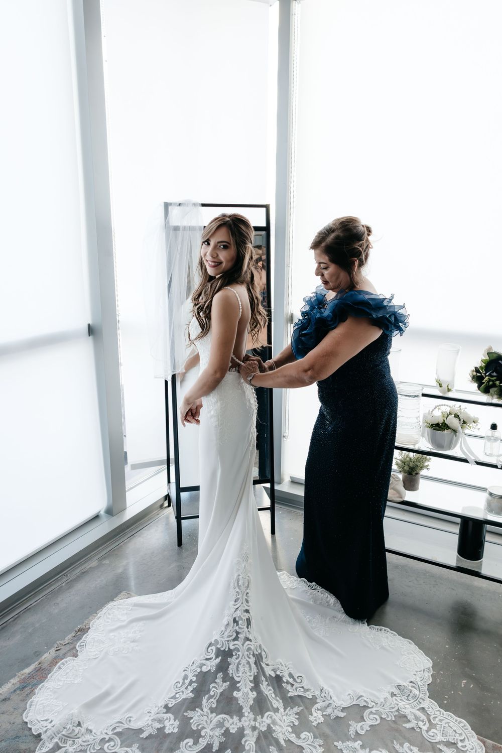 Bridal gown preparation in a minimalist white room with dramatic train details.