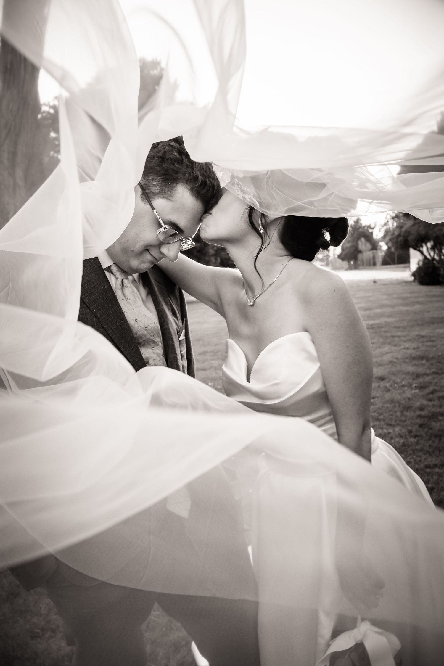 A romantic black and white wedding photo series showing tender moments between a couple under flowing white veils.