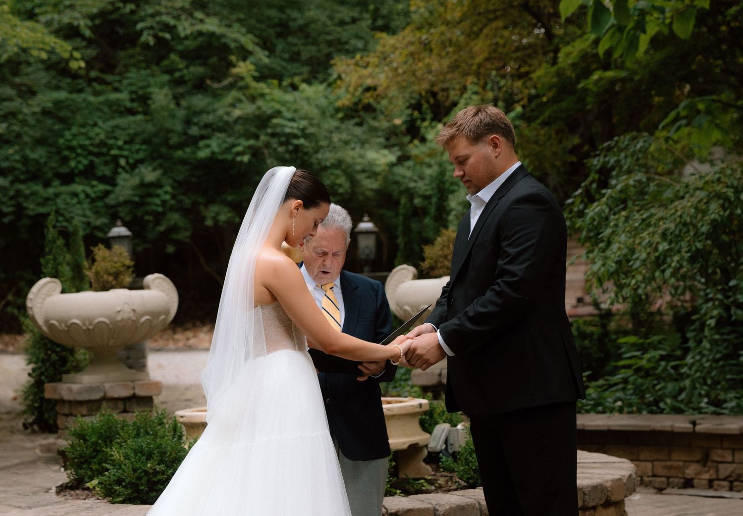 A couple shares an intimate moment during their wedding ceremony in a lush garden setting.