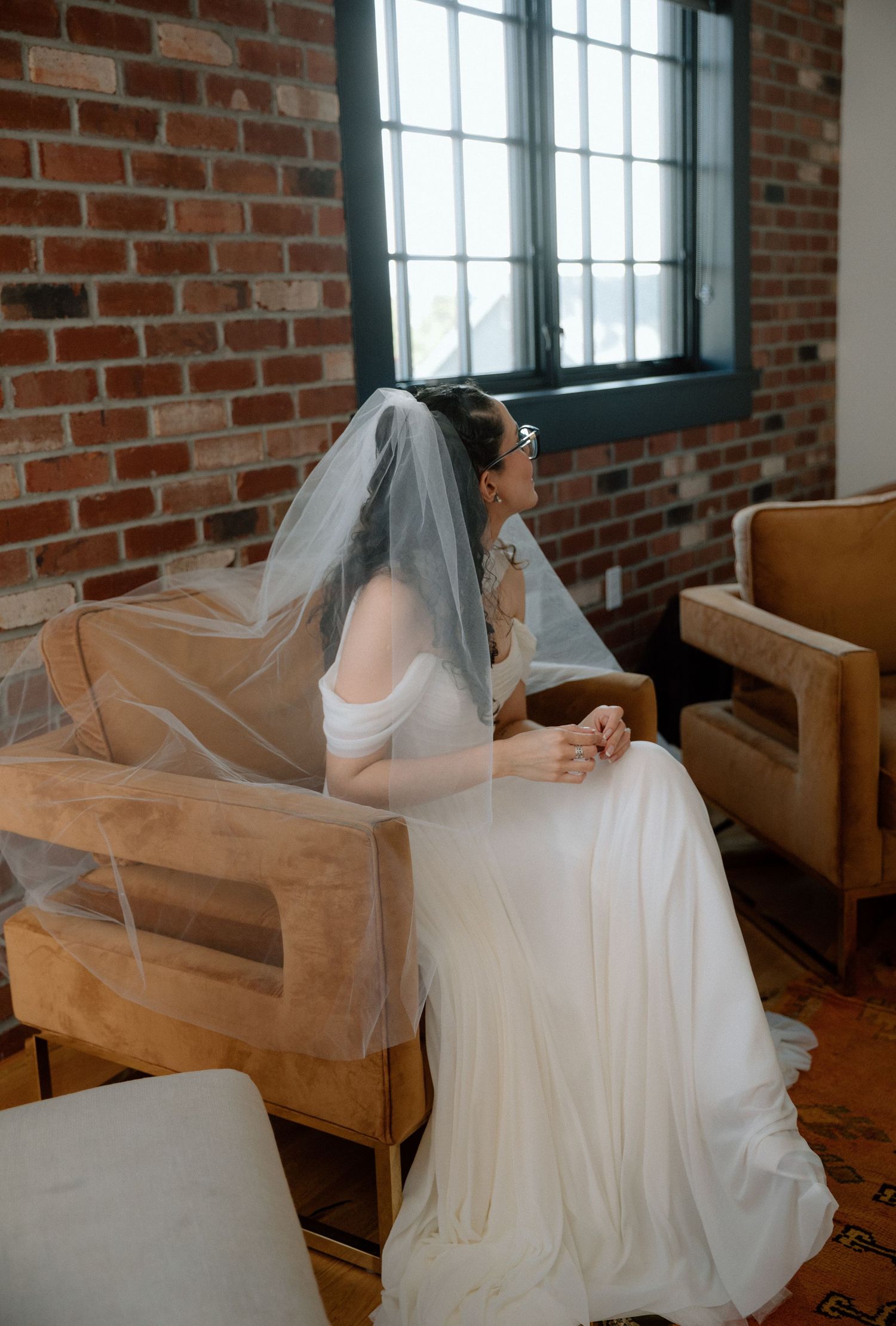 A sequence of five photos showing a bride in a flowing white dress and veil posing on a vintage brown couch against brick walls.