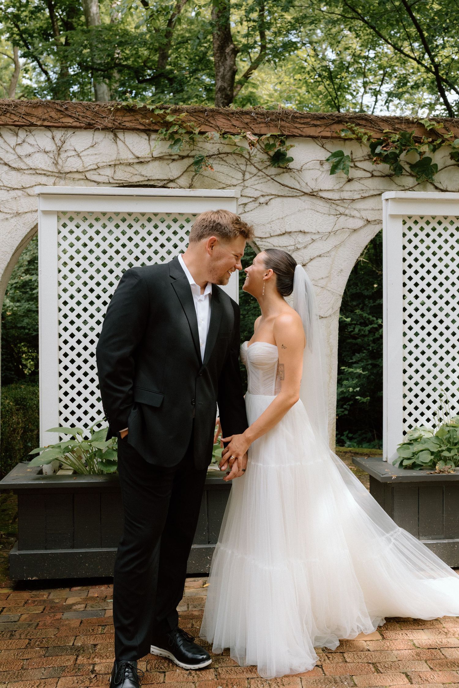 A romantic wedding couple shares intimate moments in front of a white lattice garden wall on their special day.
