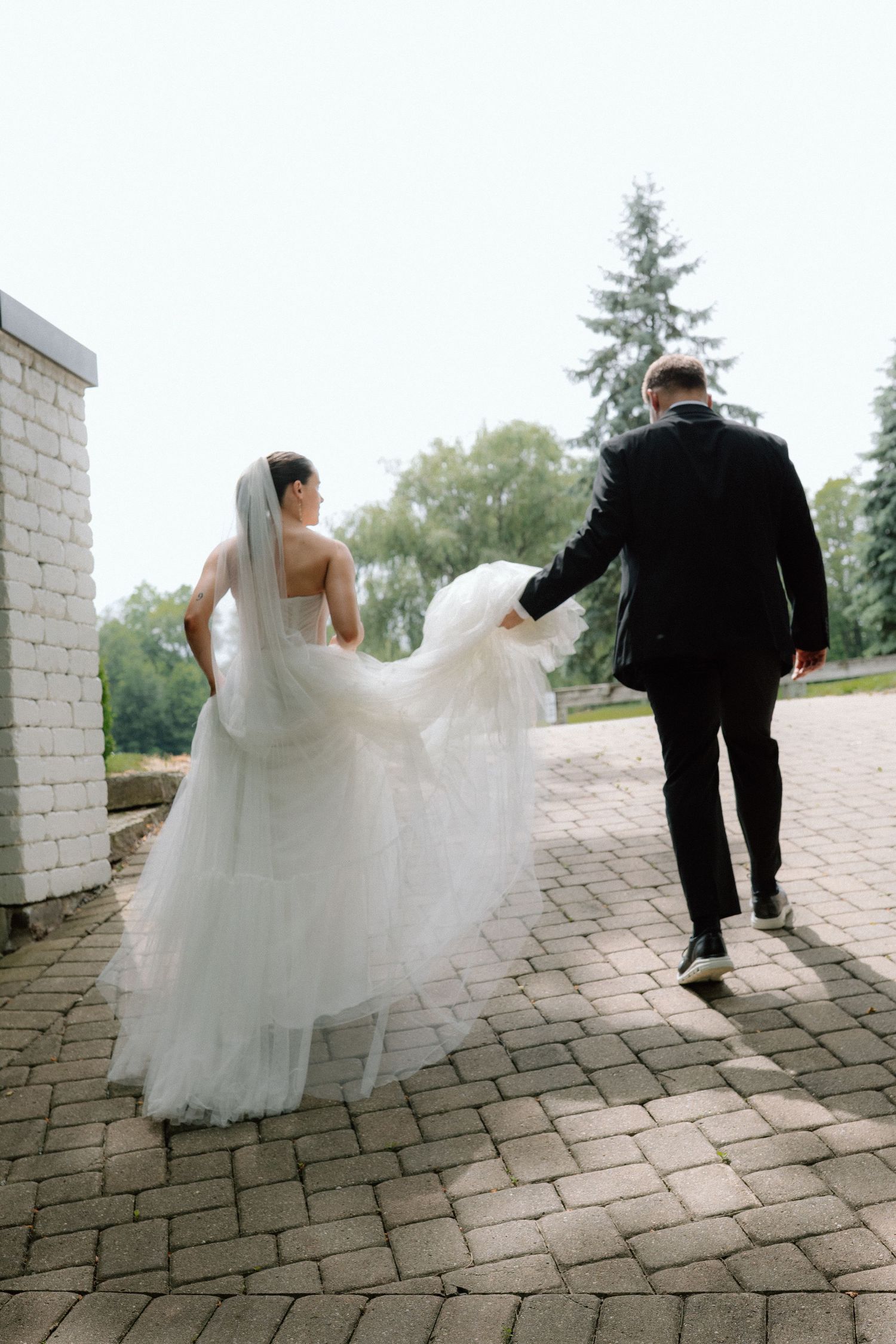 A wedding couple walks away on a stone patio surrounded by garden landscaping.