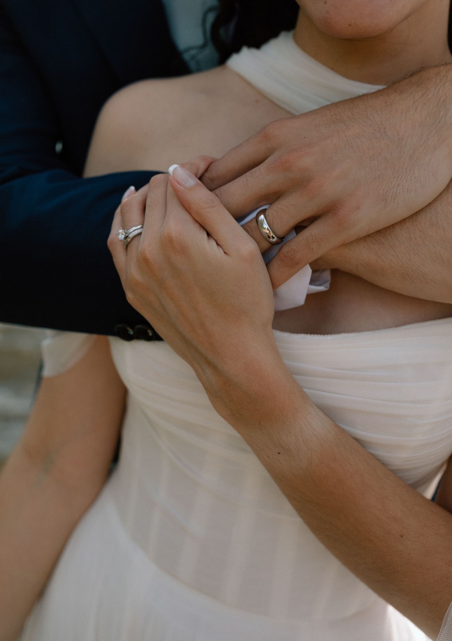 Close-up view of hands wearing engagement rings against a white dress background.