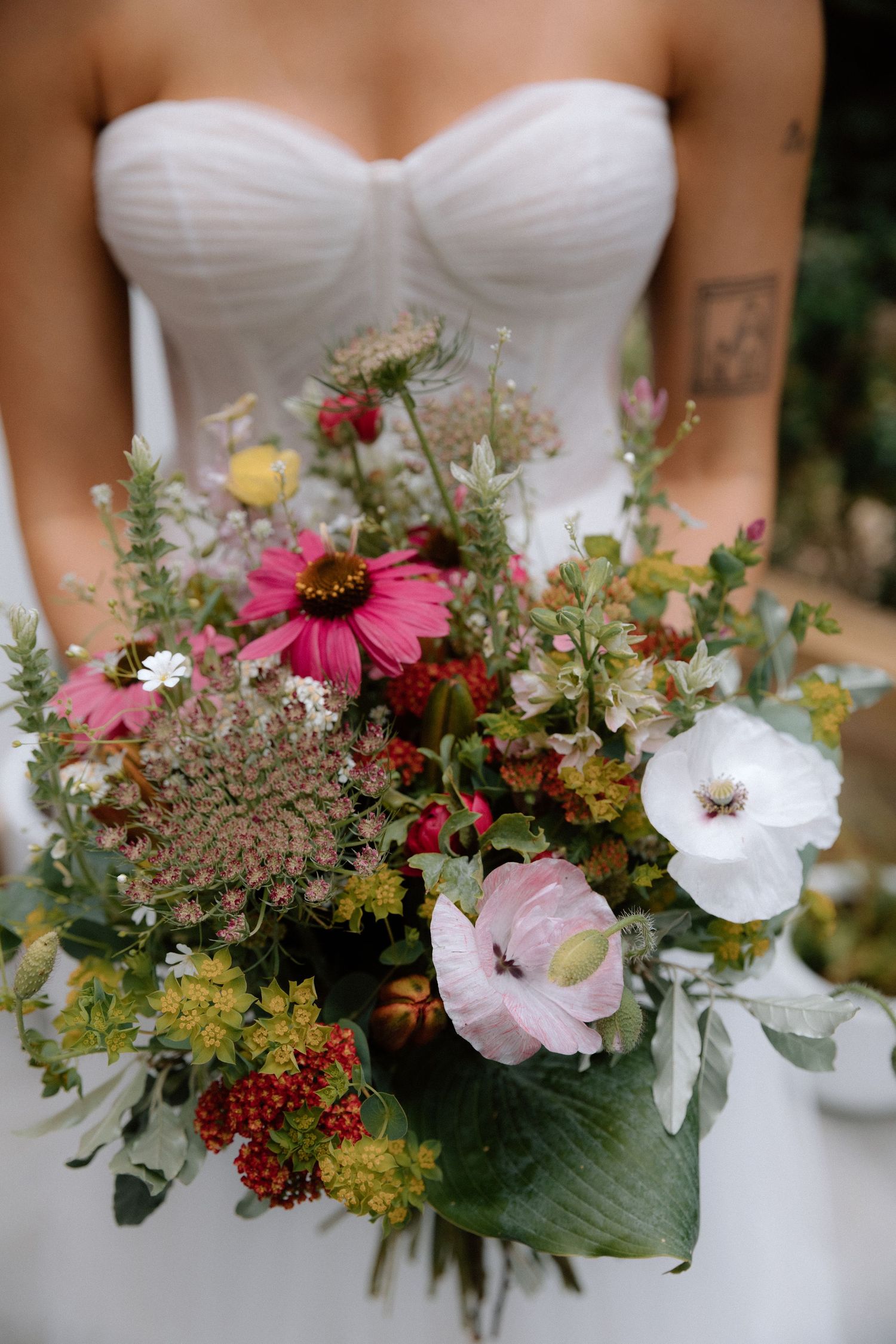 A series of wedding bouquets featuring pink coneflowers, white blooms, and mixed greenery against white dresses.